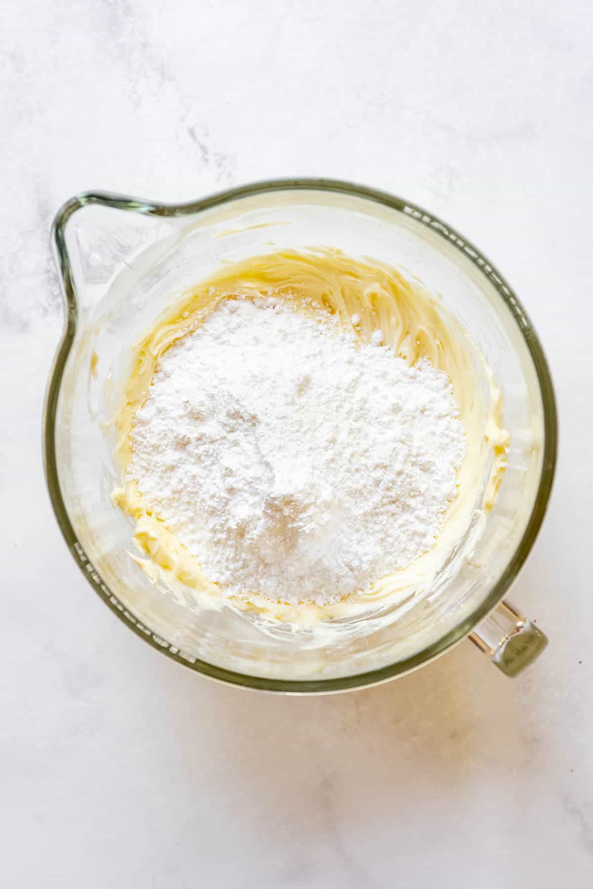 Adding powdered sugar to creamed butter and white chocolate in a mixing bowl to make frosting.