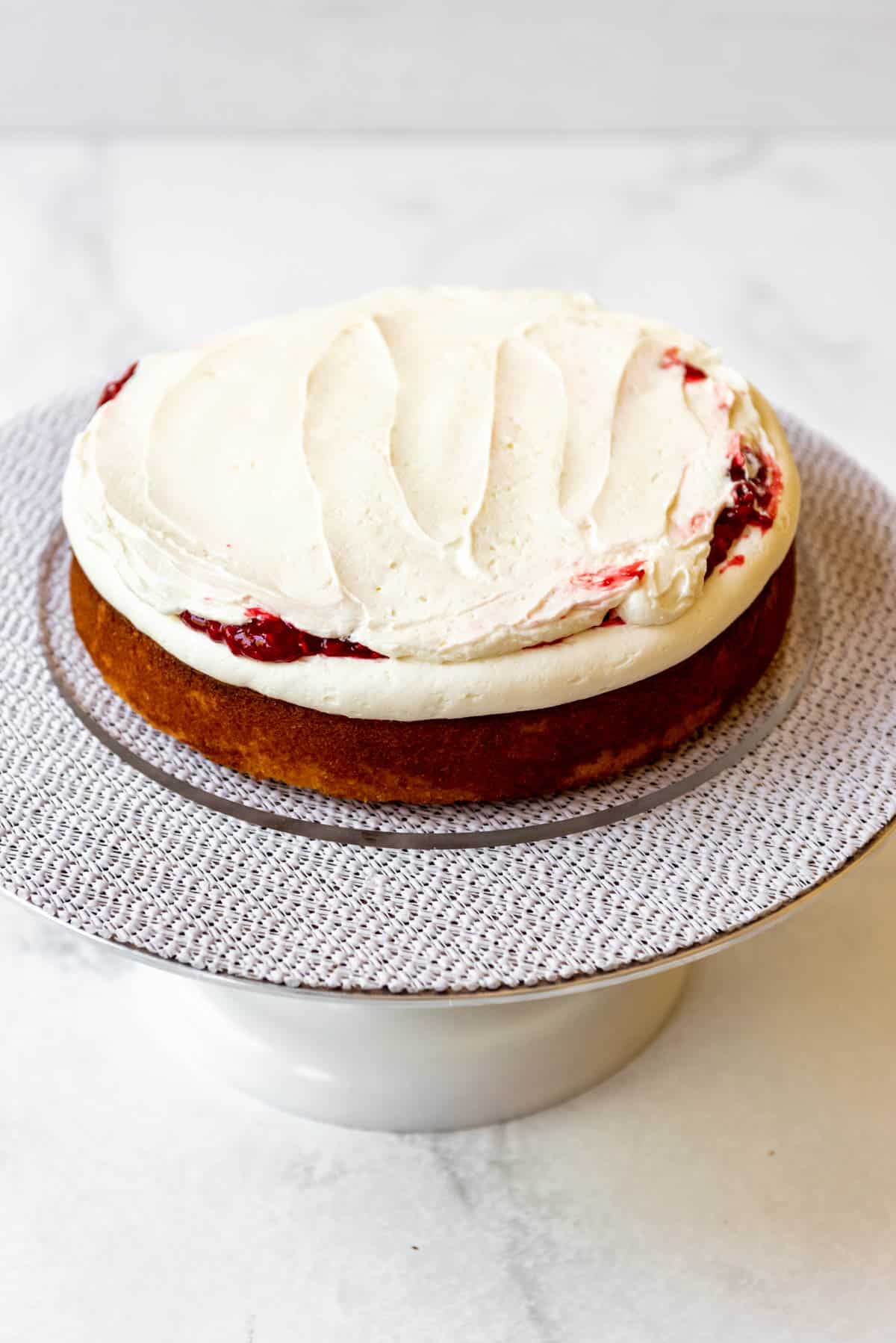 Spreading white chocolate frosting over raspberry cake filling.