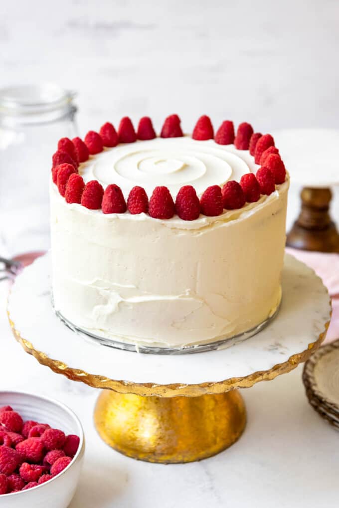 An image of a white chocolate raspberry cake decorated with whole raspberries on top.
