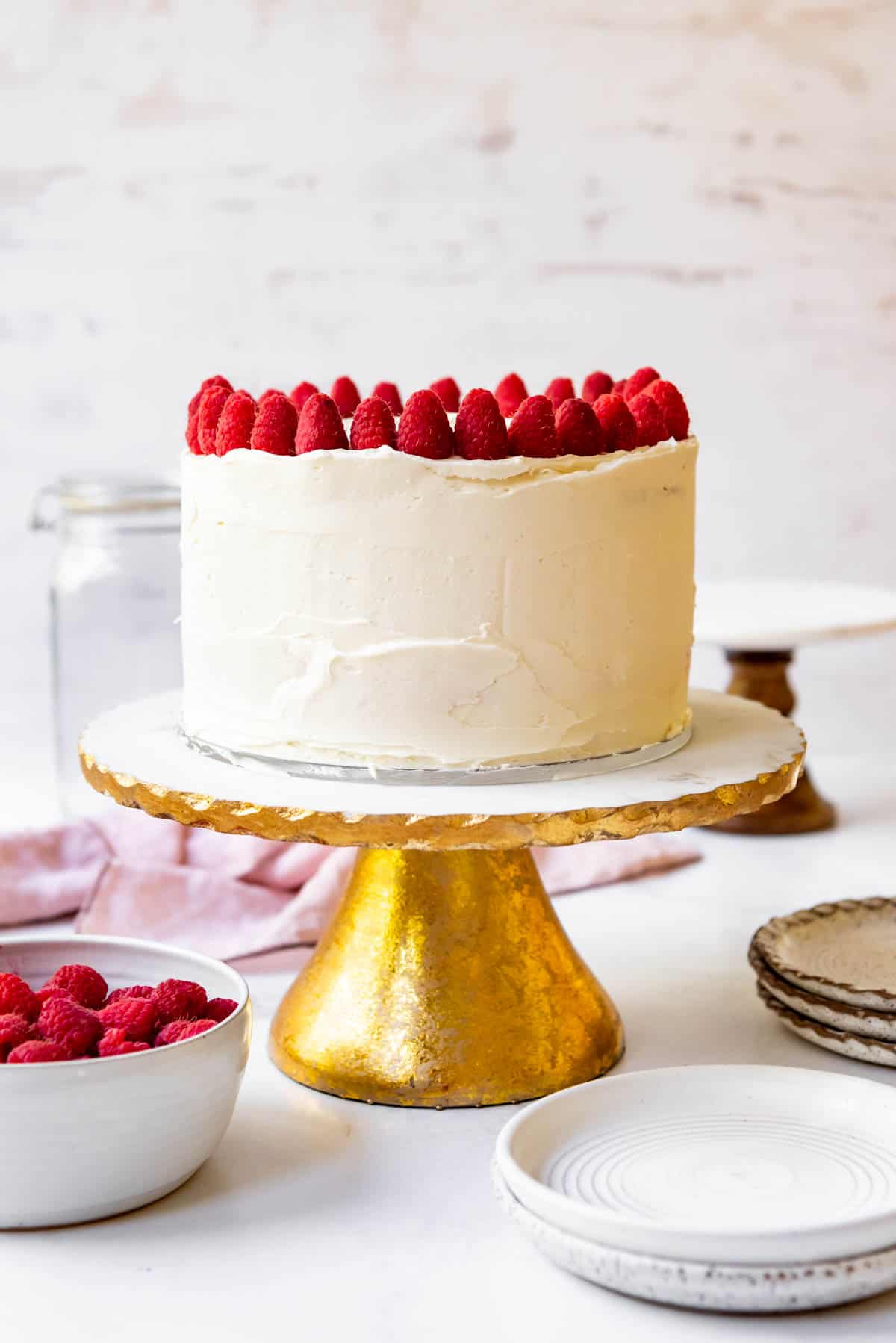 A whole white chocolate raspberry layer cake on a gold cake stand.