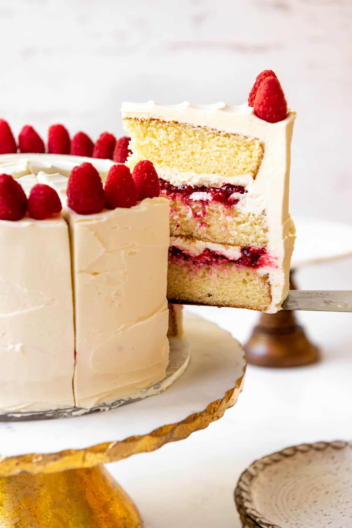 A slice of white chocolate raspberry cake being lifted out of a whole cake.