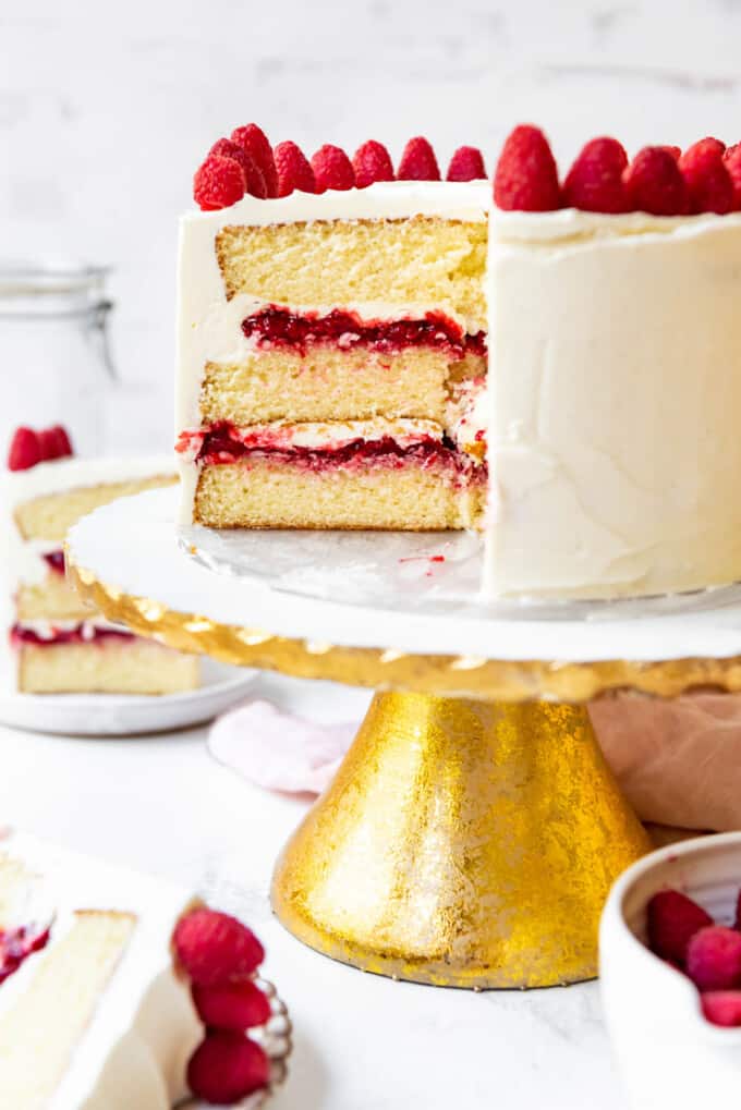 A white chocolate raspberry layer cake on a gold and white marble cake stand.