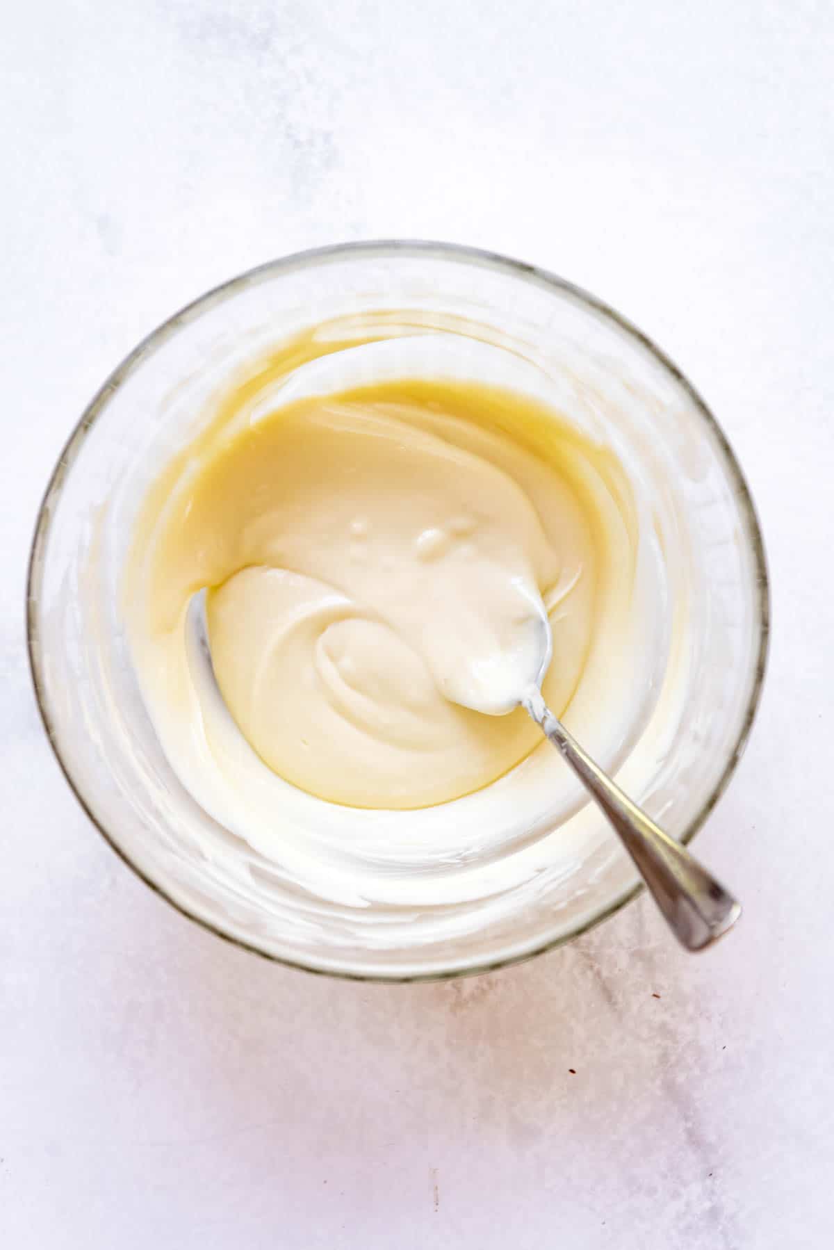 Melted white chocolate in a glass bowl with a spoon.