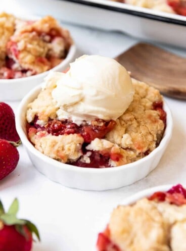 A bowl of strawberry rhubarb cobbler with a scoop of vanilla ice cream on top.