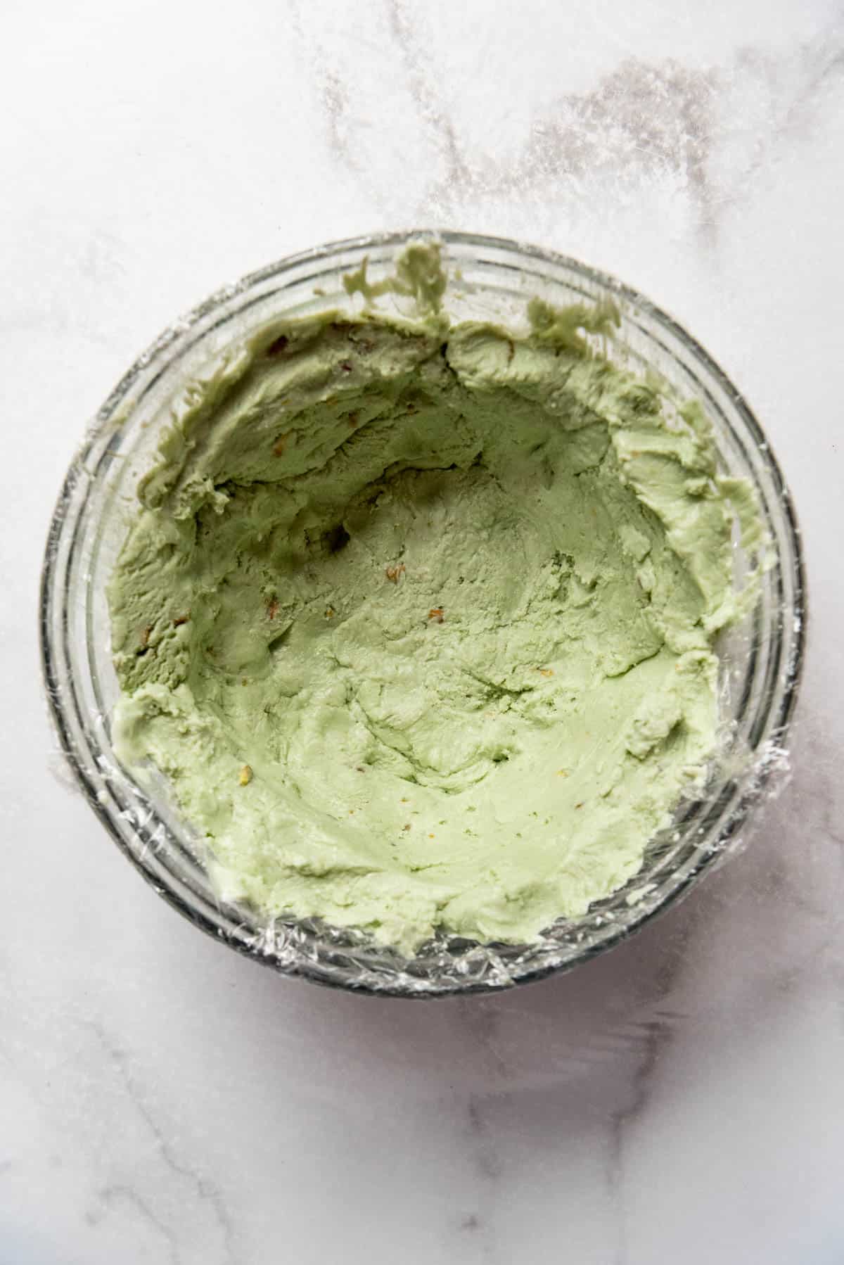 Molding softened pistachio ice cream around the edges of a glass bowl.