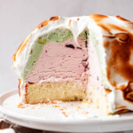 A baked Alaska on a white cake stand with pistachio and cherry flavors.