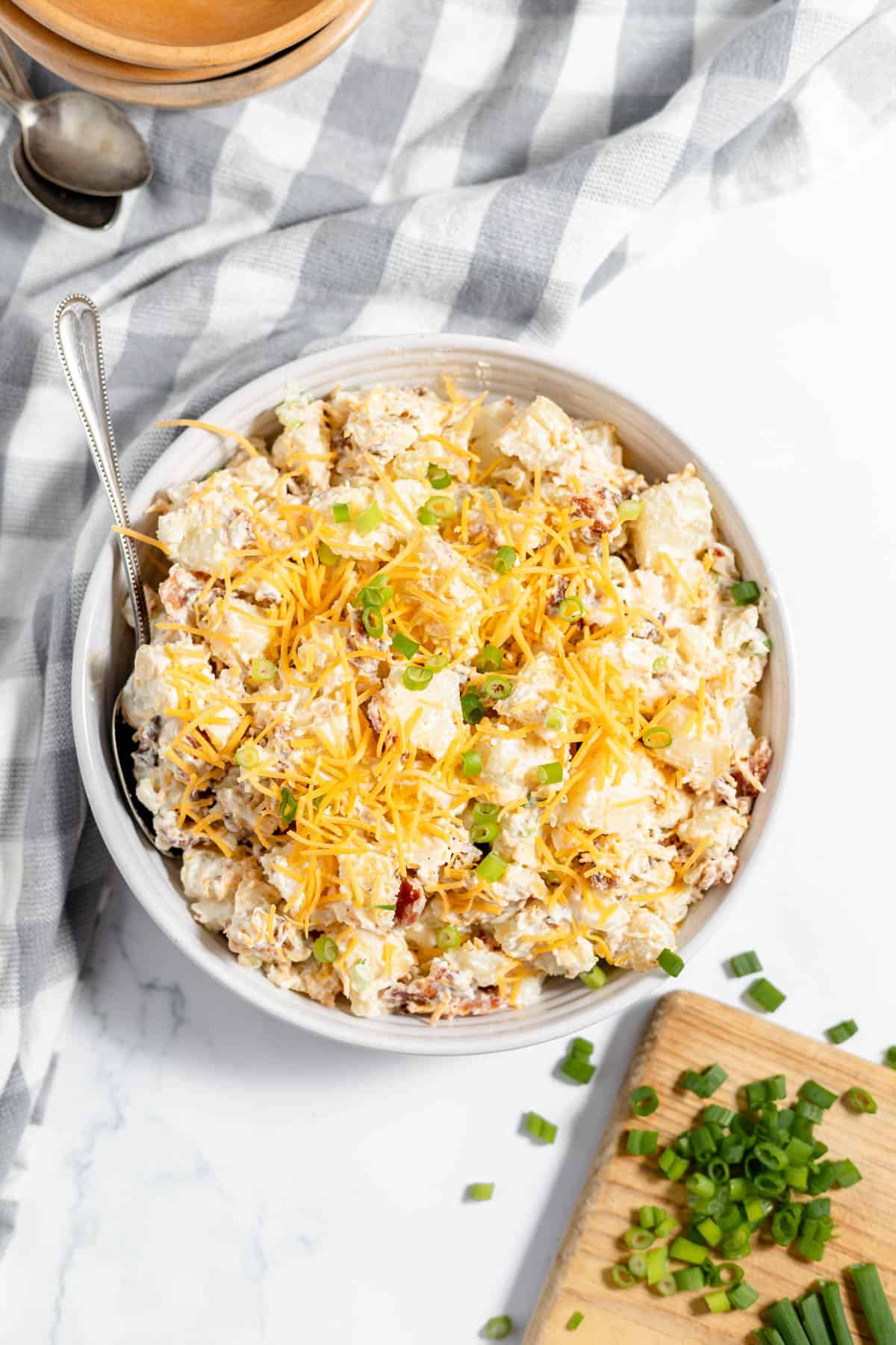 A bowl of loaded baked potato salad with grated cheese sprinkled on top.
