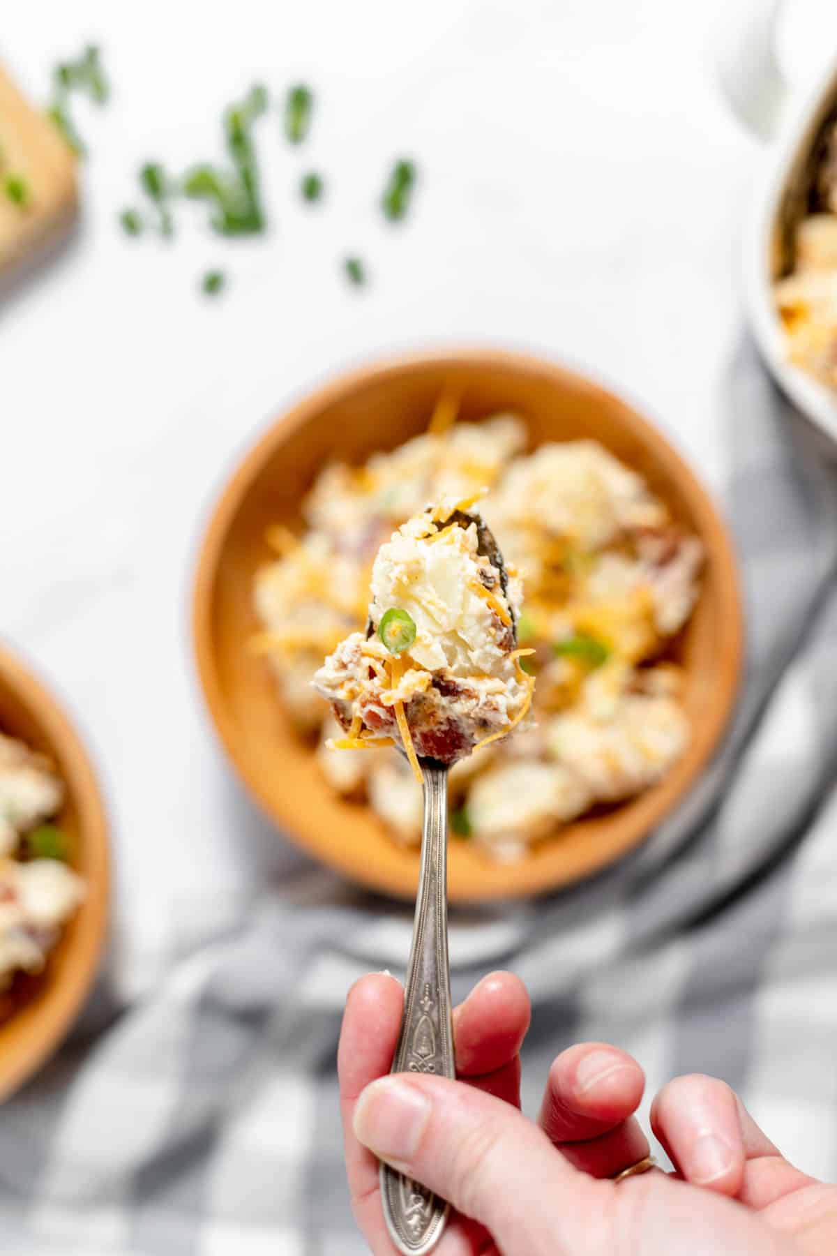 A spoonful of loaded baked potato salad held over the bowl.
