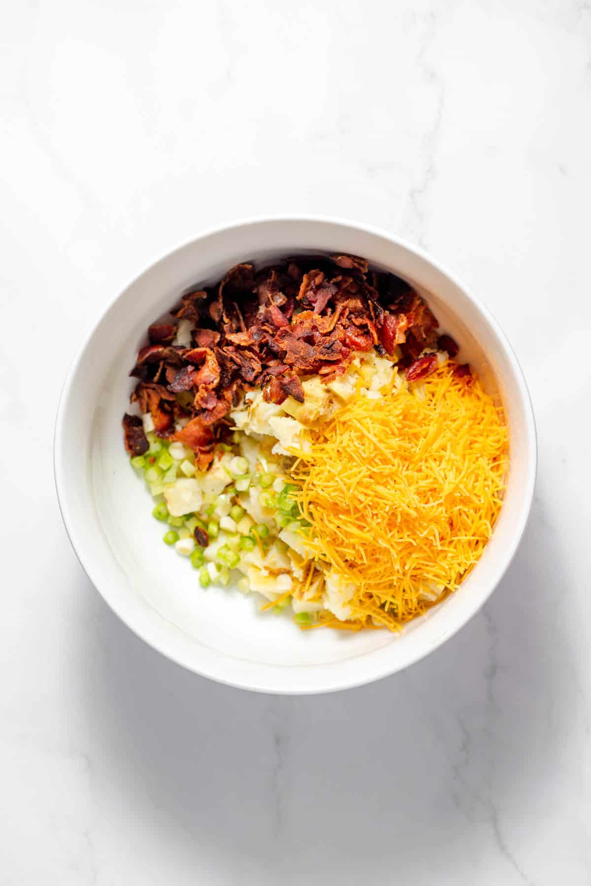Combining chopped baked potato, shredded cheese, green onion, and bacon in a large bowl.