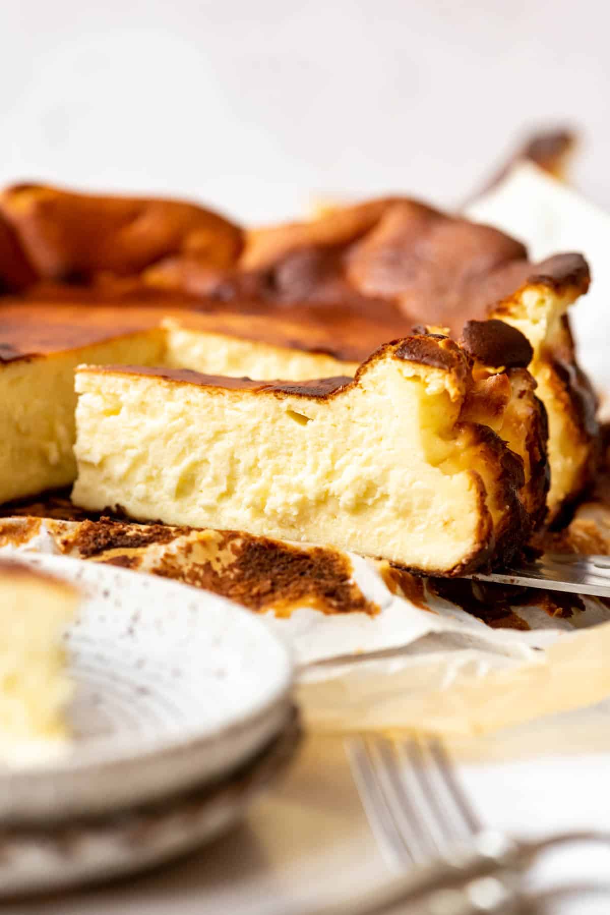 A slice of creamy Basque cheesecake next to the rest of the cheesecake.