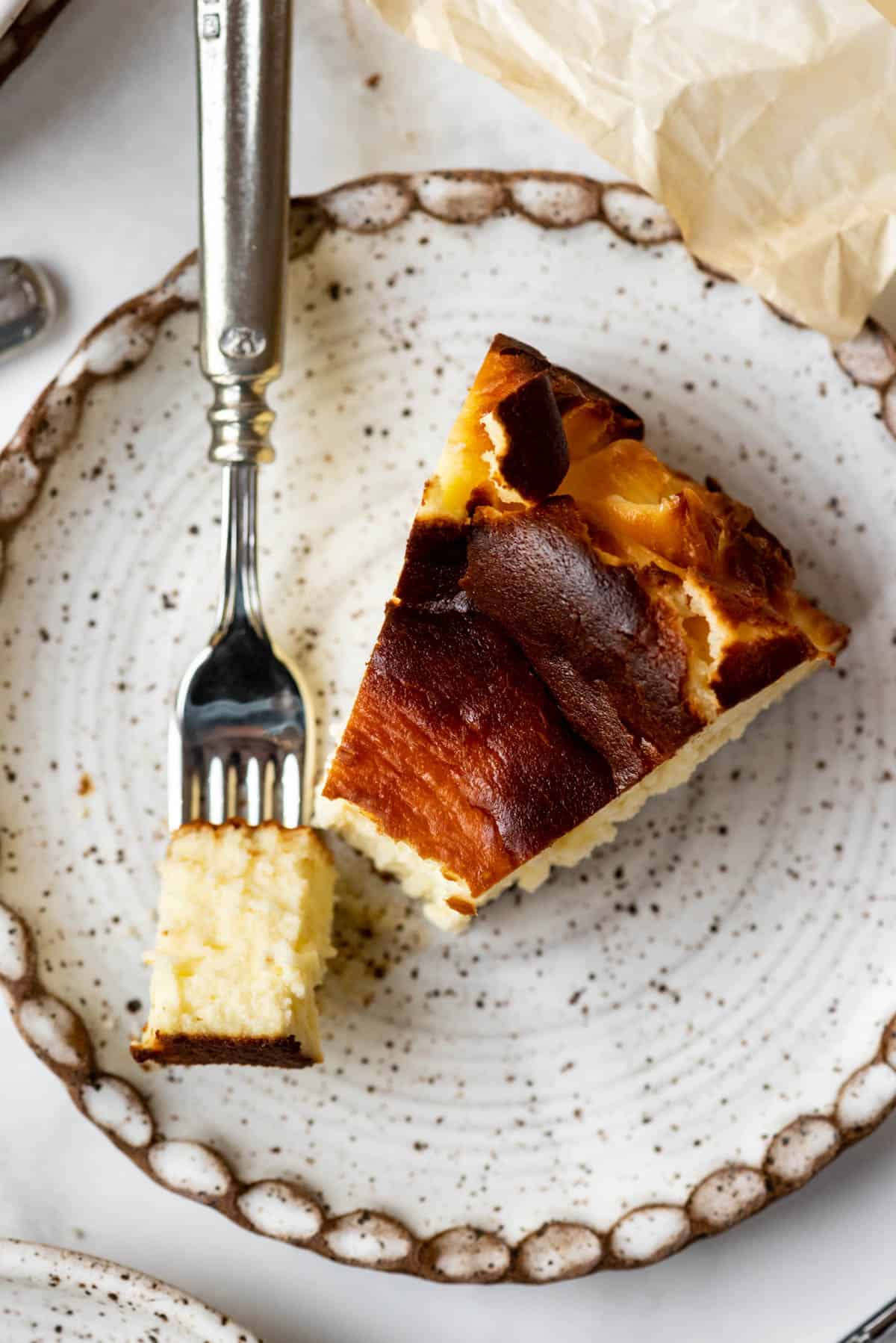 A bite of Basque cheesecake on a fork next to the slice of cheesecake on a plate.