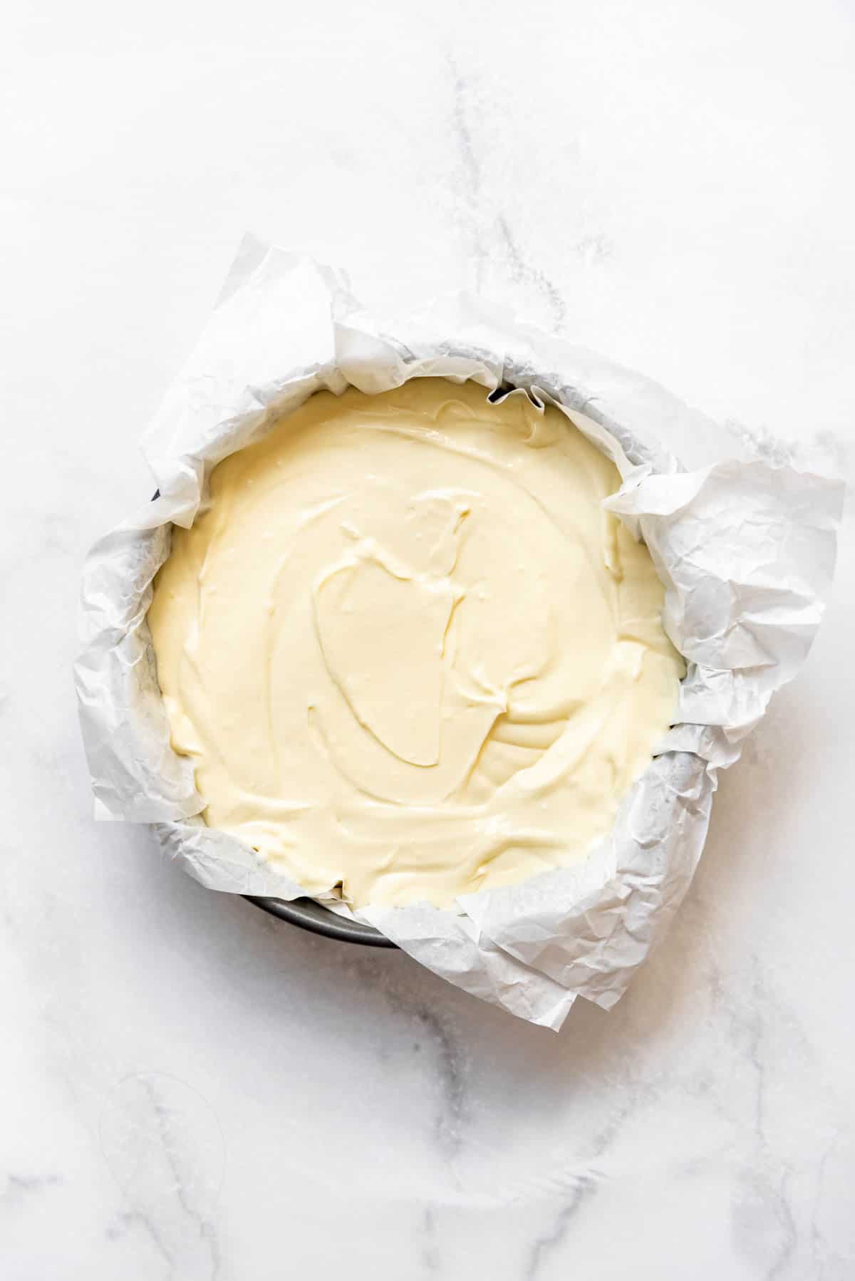Basque cheesecake batter poured into a 9-inch springform pan lined with parchment paper.