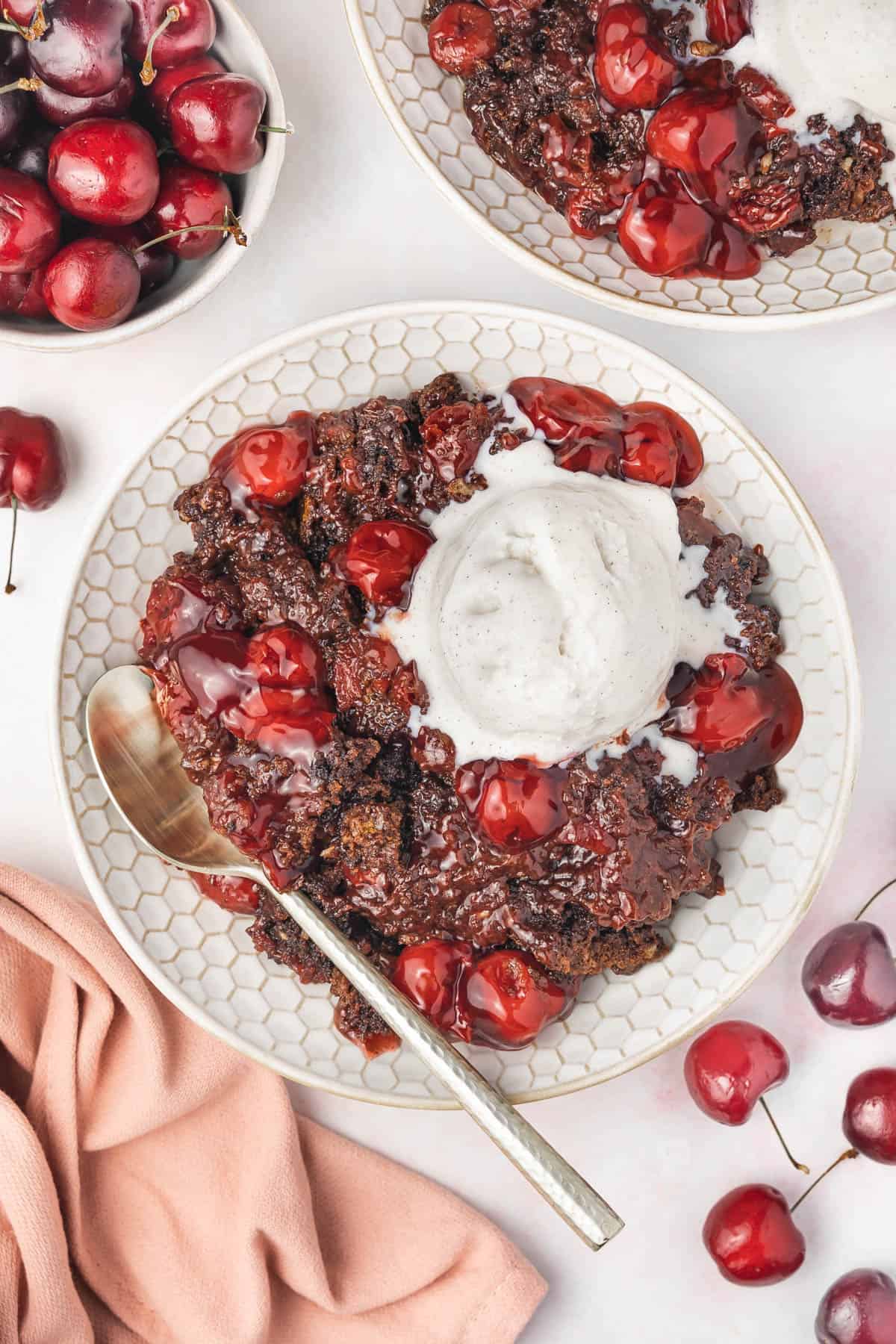 An overhead image of a bowl of chocolate cherry dump cake with a scoop of vanilla ice cream.