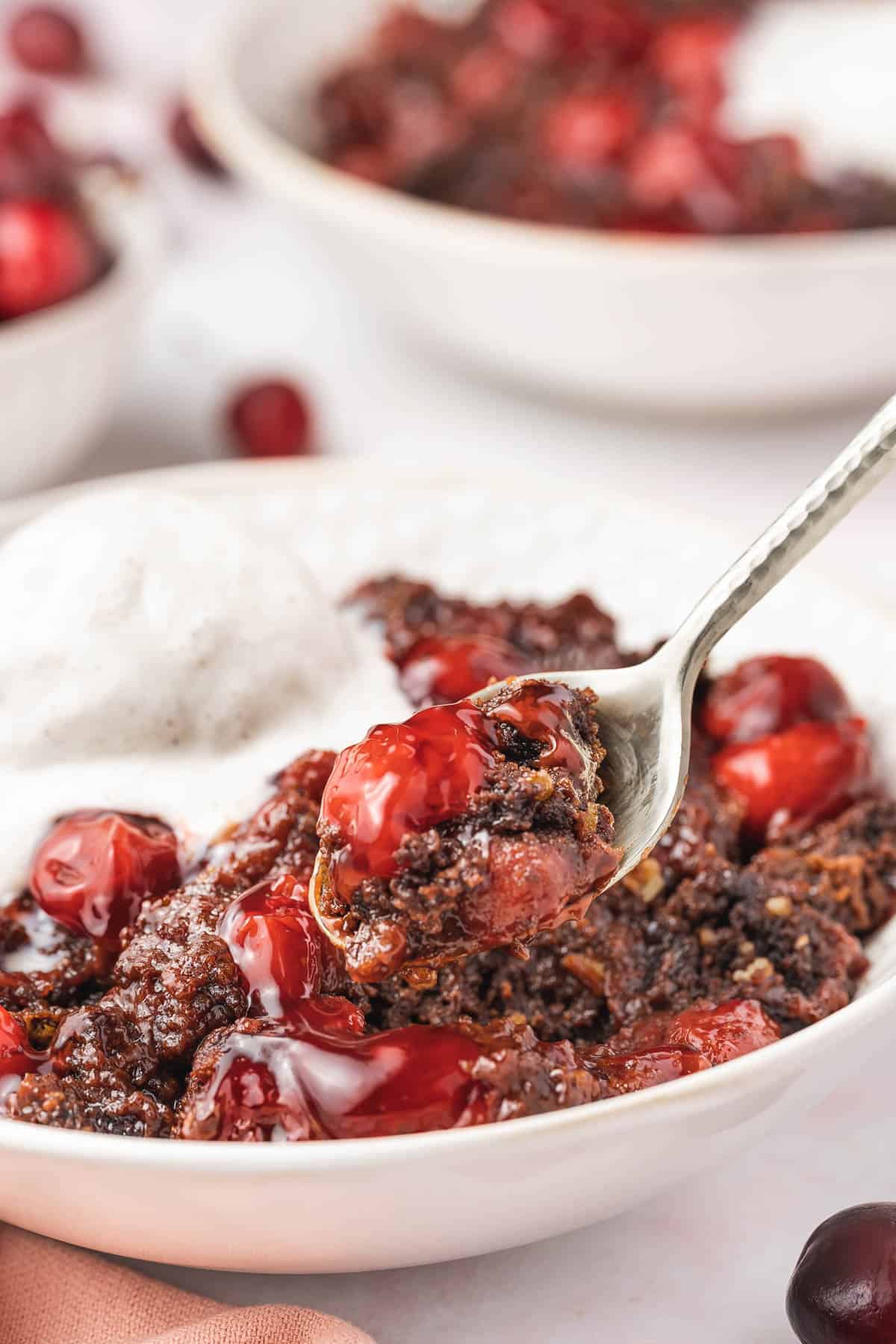 A spoon lifting chocolate cherry dump cake from a bowl. 