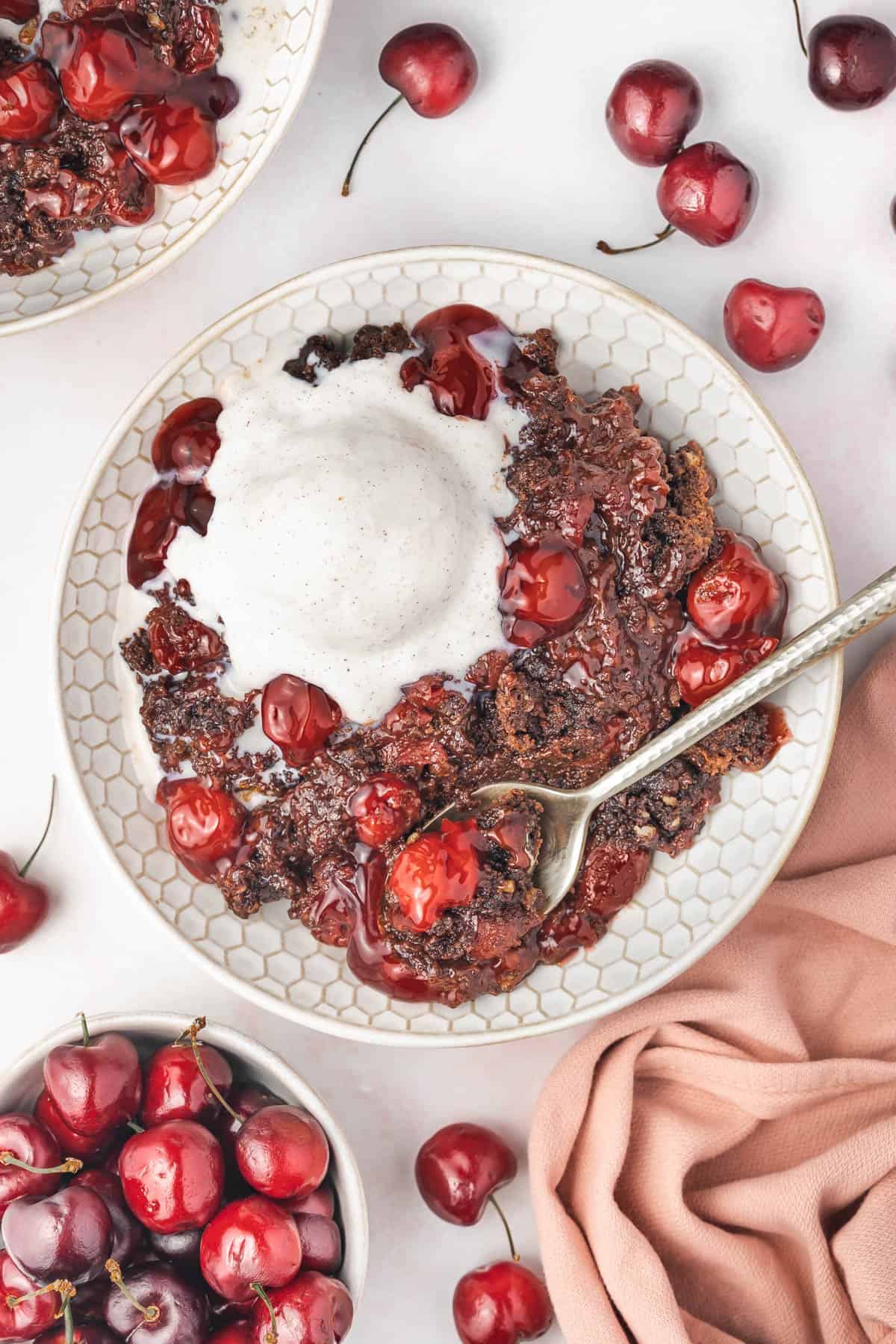 A bowl of chocolate cherry dump cake with a spoon in it.