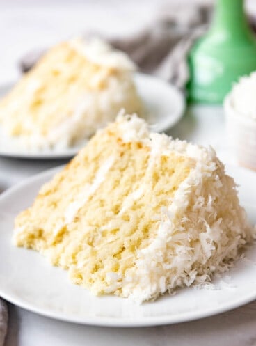 A slice of moist homemade coconut cake from scratch on a white plate.