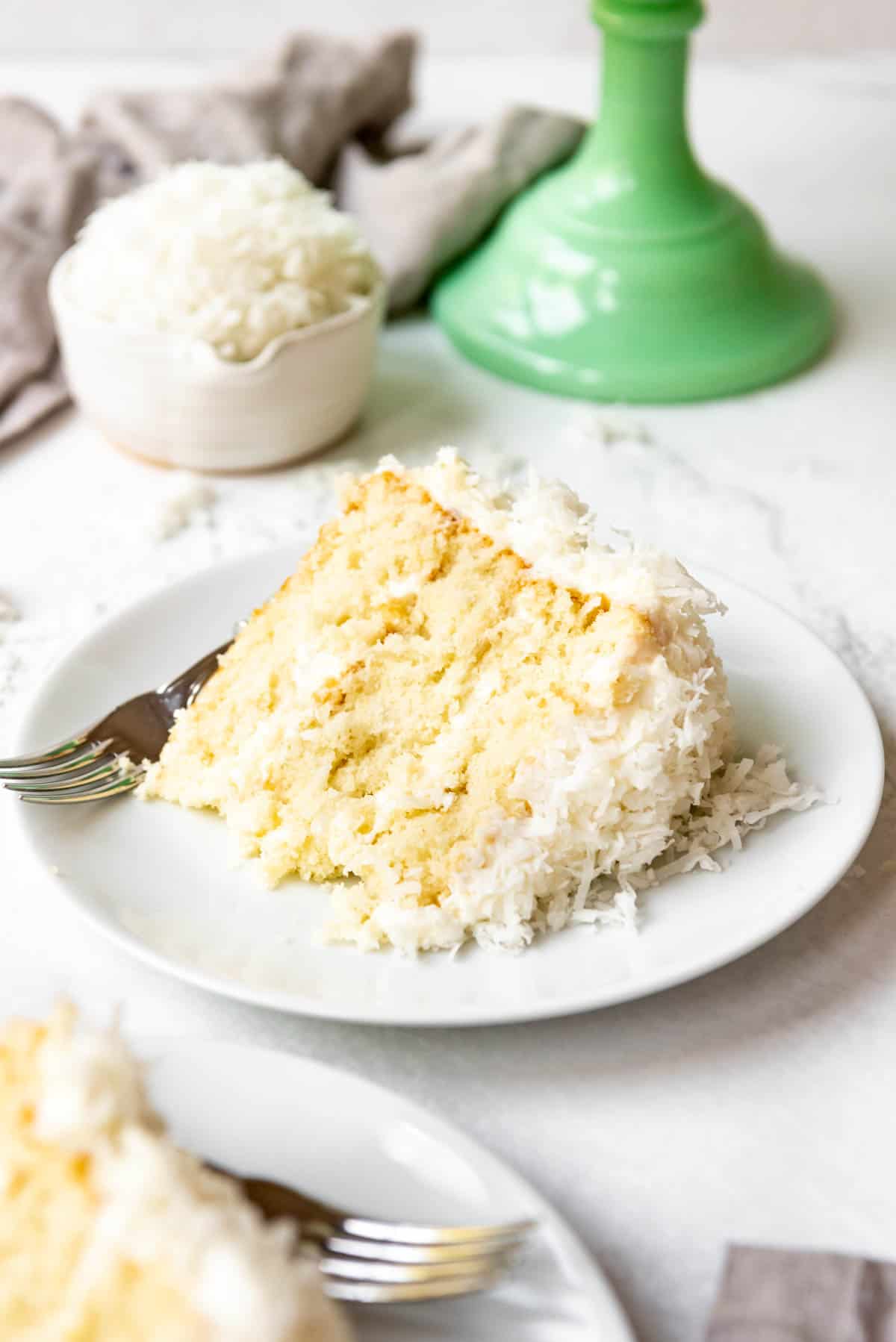 A slice of coconut cake on a white plate with a fork.