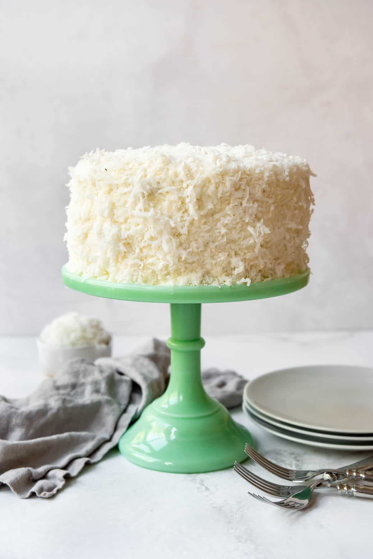 A green cake stand with a frosted and coconut-covered cake on top.