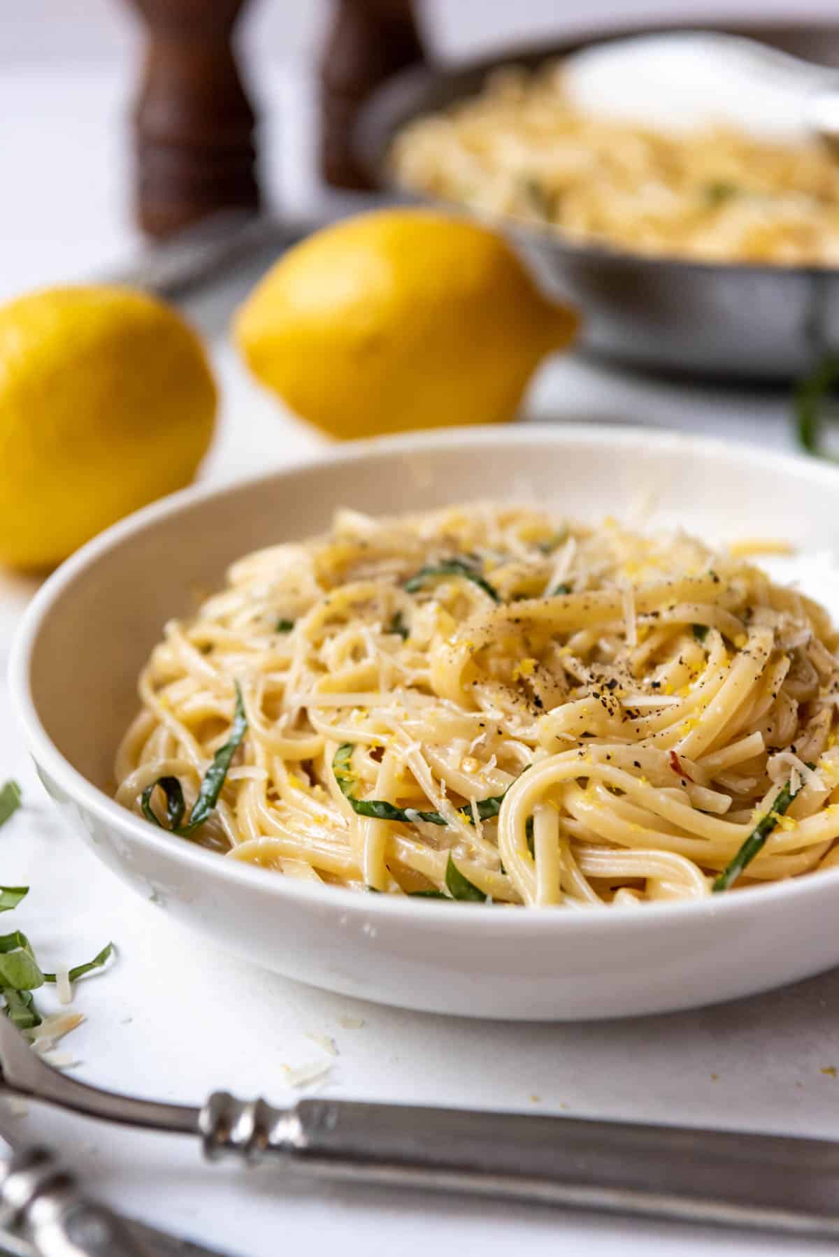 A bowl of creamy lemon pasta in front of whole lemons.