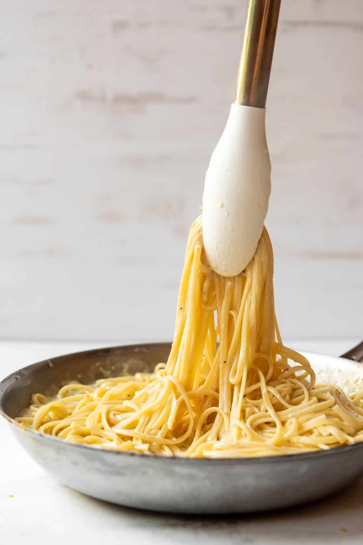 Tossing pasta with a creamy lemon sauce using tongs.