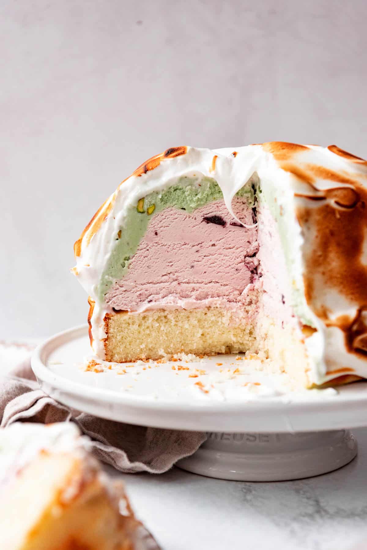 A baked Alaska on a white cake stand with pistachio and cherry flavors.