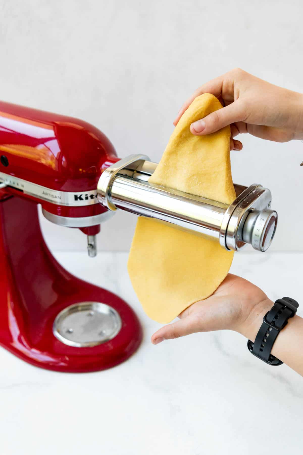 A sheet of fresh pasta dough coming out of a pasta roller KitchenAid attachment.