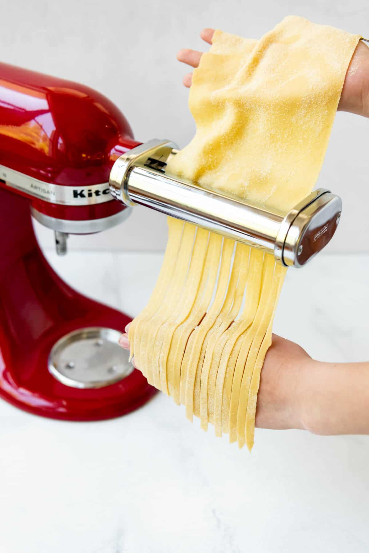 Fresh fettuccine pasta coming through a pasta roller KitchenAid attachment.