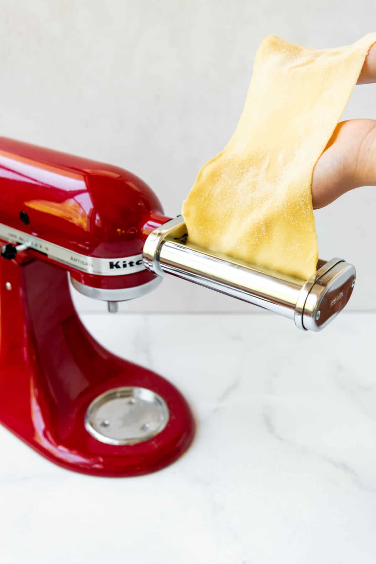 Feeding a thin sheet of fresh pasta into a pasta roller attachment for cutting fettuccine pasta noodles.