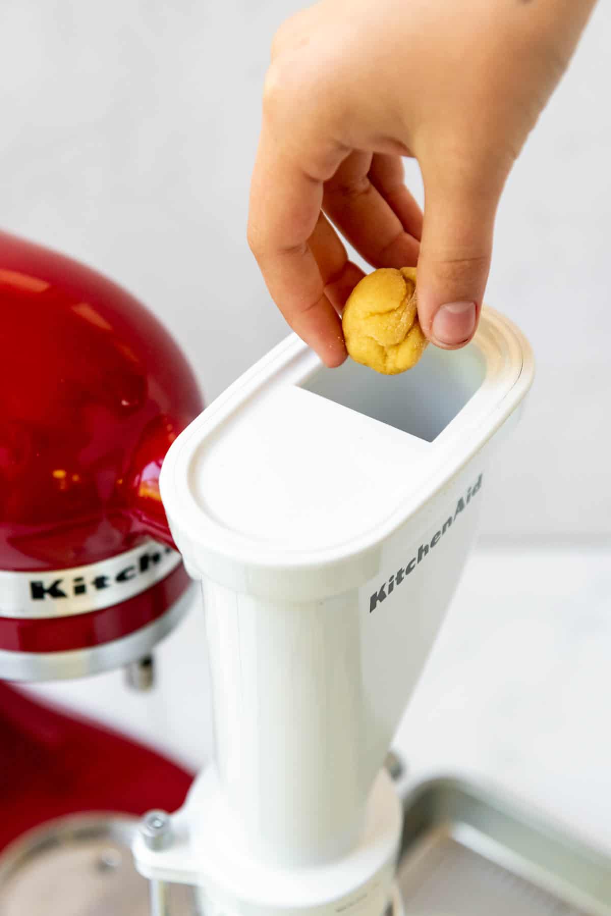 Adding a walnut sized ball of homemade pasta dough to a KitchenAid pasta extruder attachment.