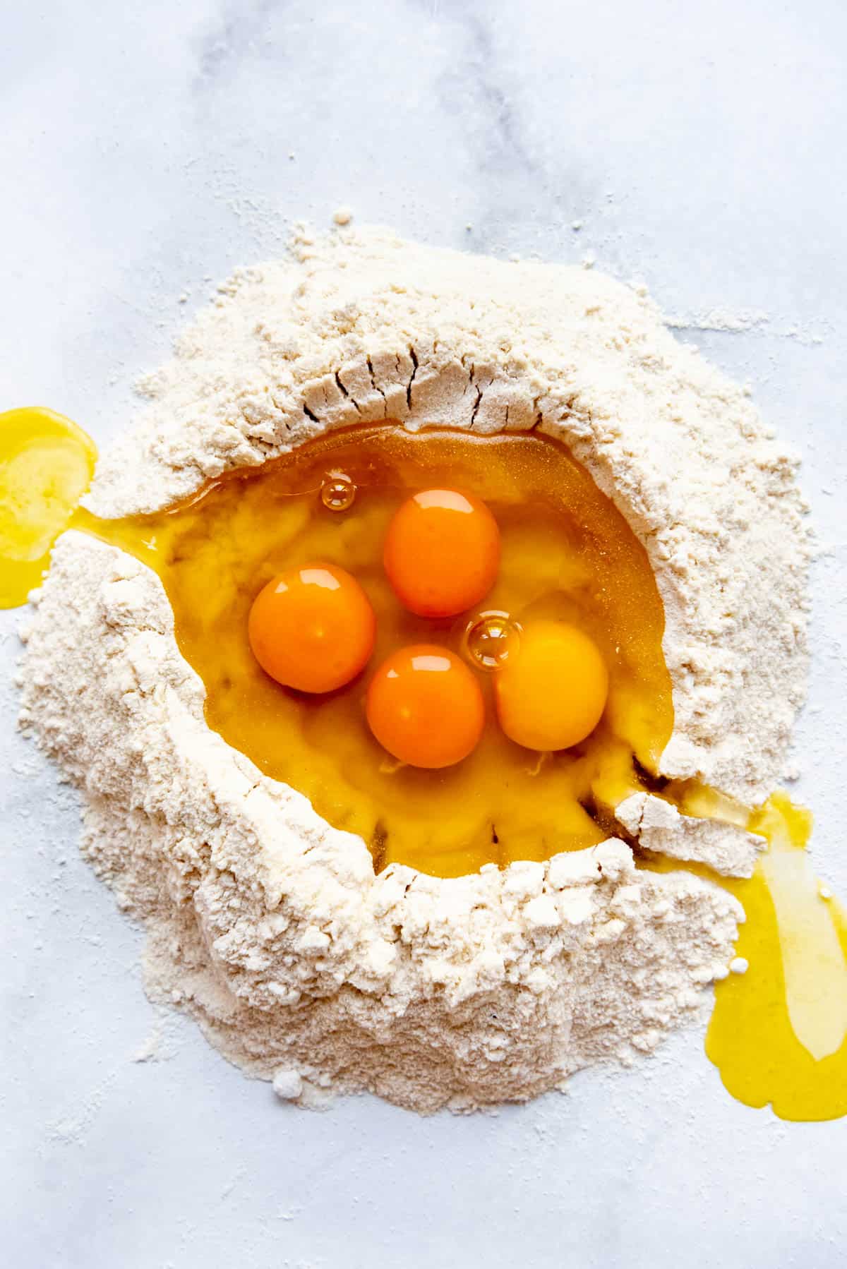 Adding whole eggs and olive oil to a well in the middle of a pile of semolina and all-purpose flour for making homemade pasta.