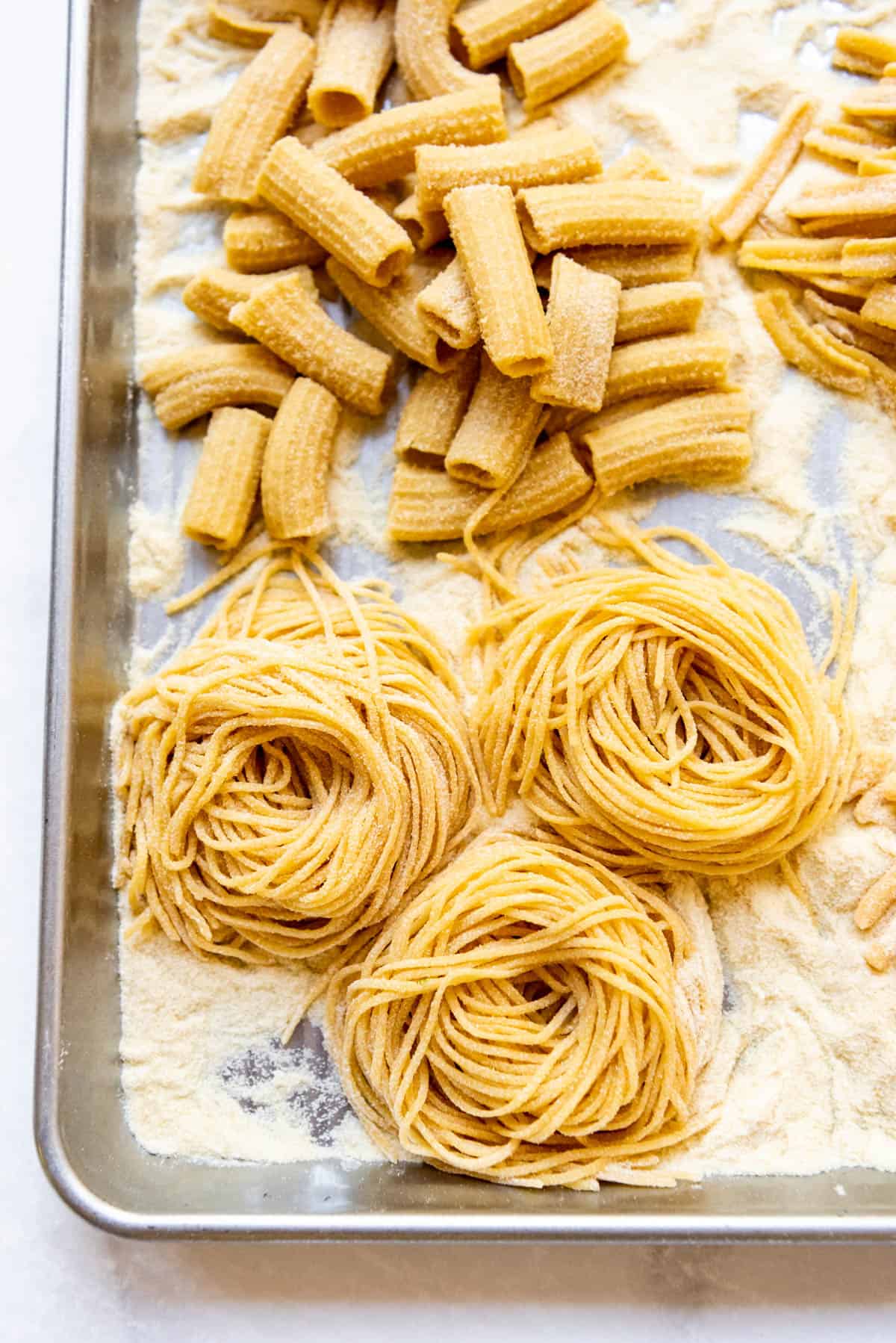 A close image of homemade fresh spaghetti twirled into nests on a baking sheet.