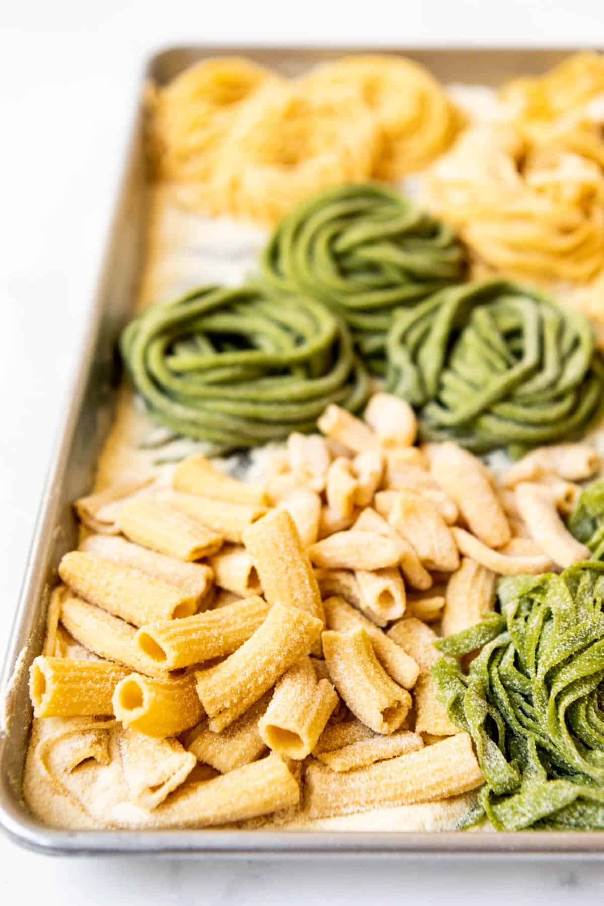 Homemade rigatoni pasta noodles next to spinach pasta in other shapes.
