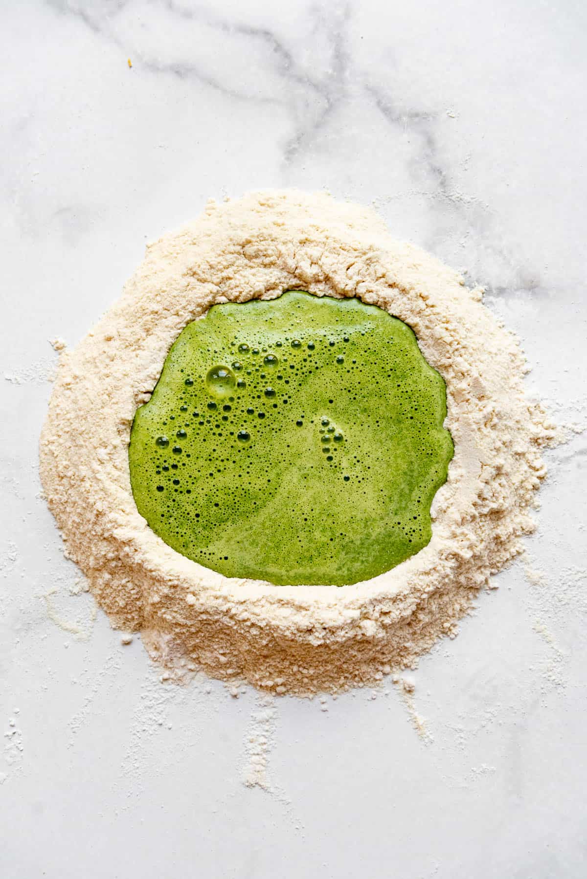 Adding blended spinach and eggs to a well of flour for making pasta dough.