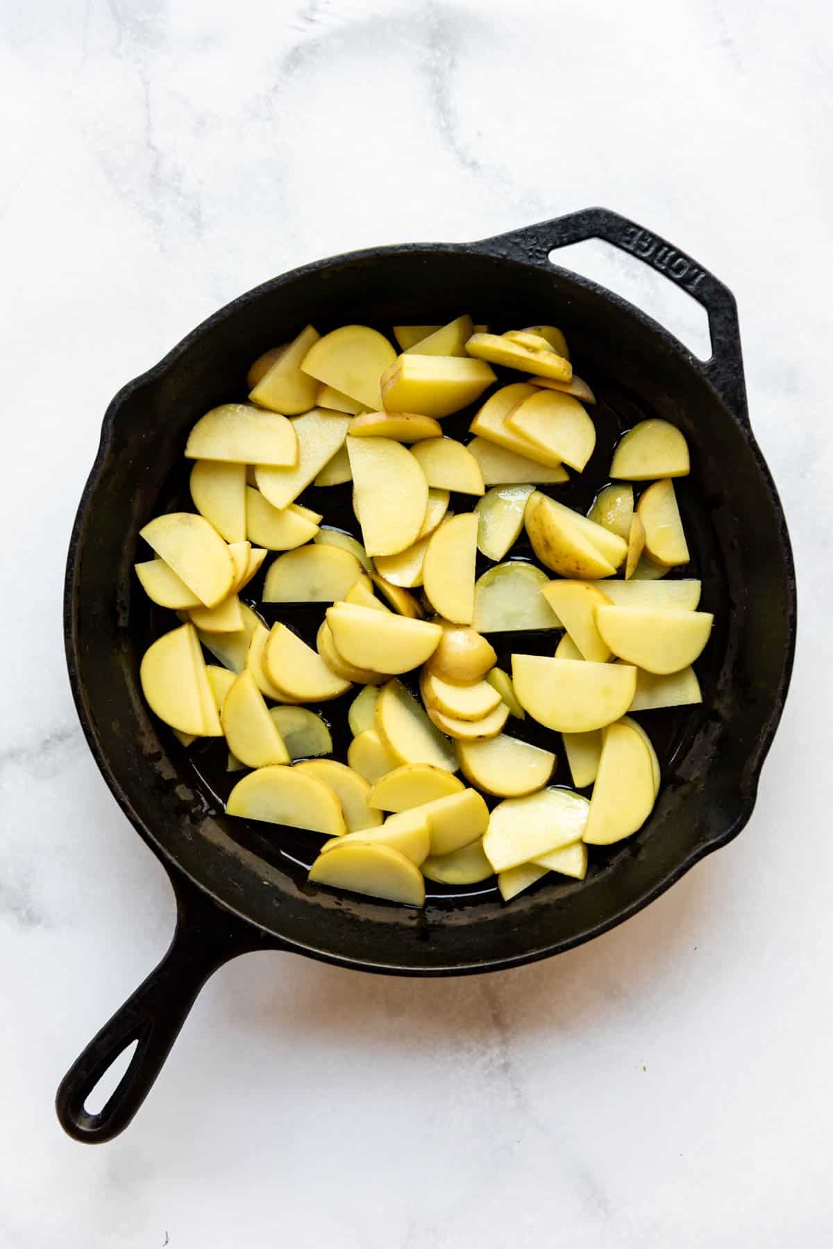 Frying sliced potatoes in oil in a cast iron skillet.