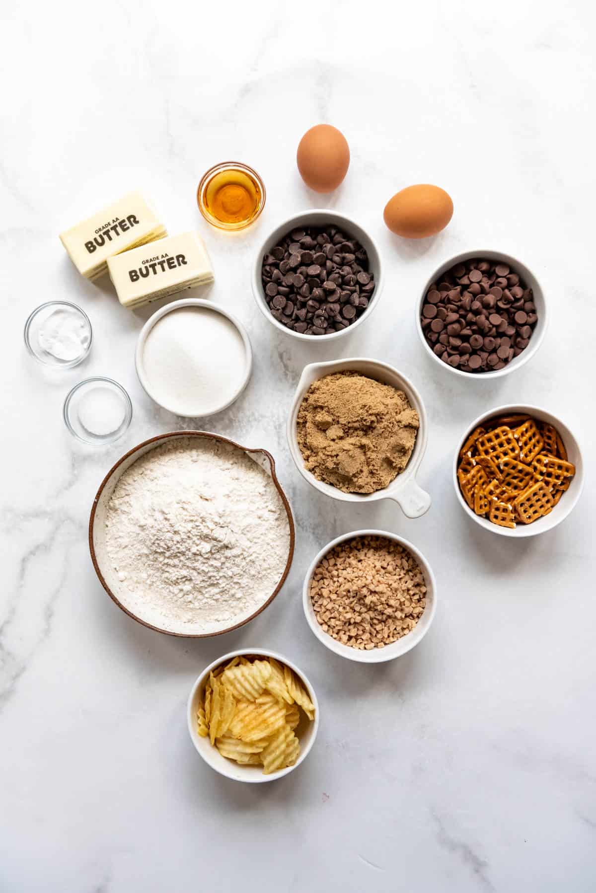 Top view of ingredients needed to make kitchen sink cookies in small bowls on a white surface.