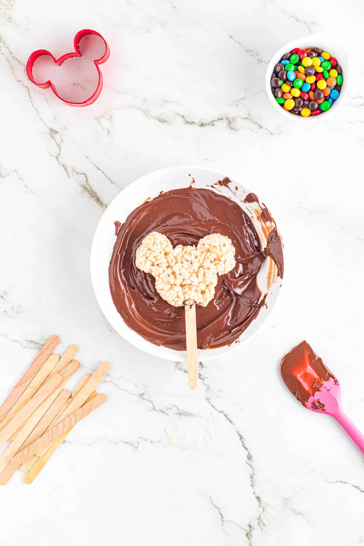 Dipping Mickey-shaped rice krispies treats into melted chocolate.