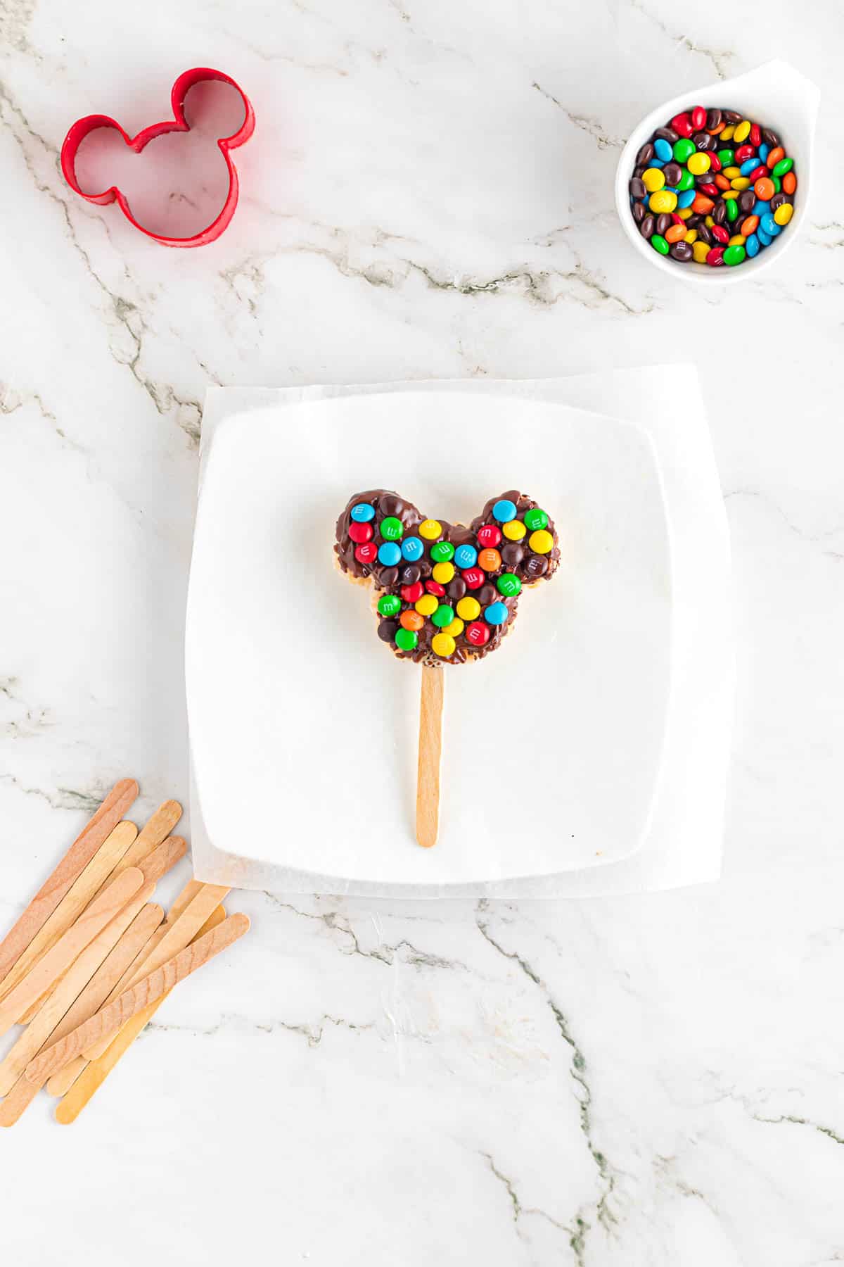 A mickey rice krispy treat that has been dipped in chocolate and pressed in mini M&M's.