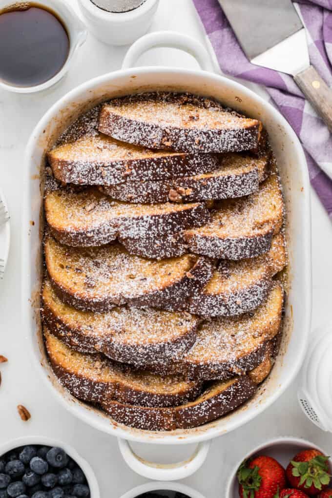 Finished overnight French toast dusted with powdered sugar in a baking dish.