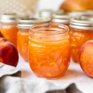 Jars of peach jam with the front jar opened.