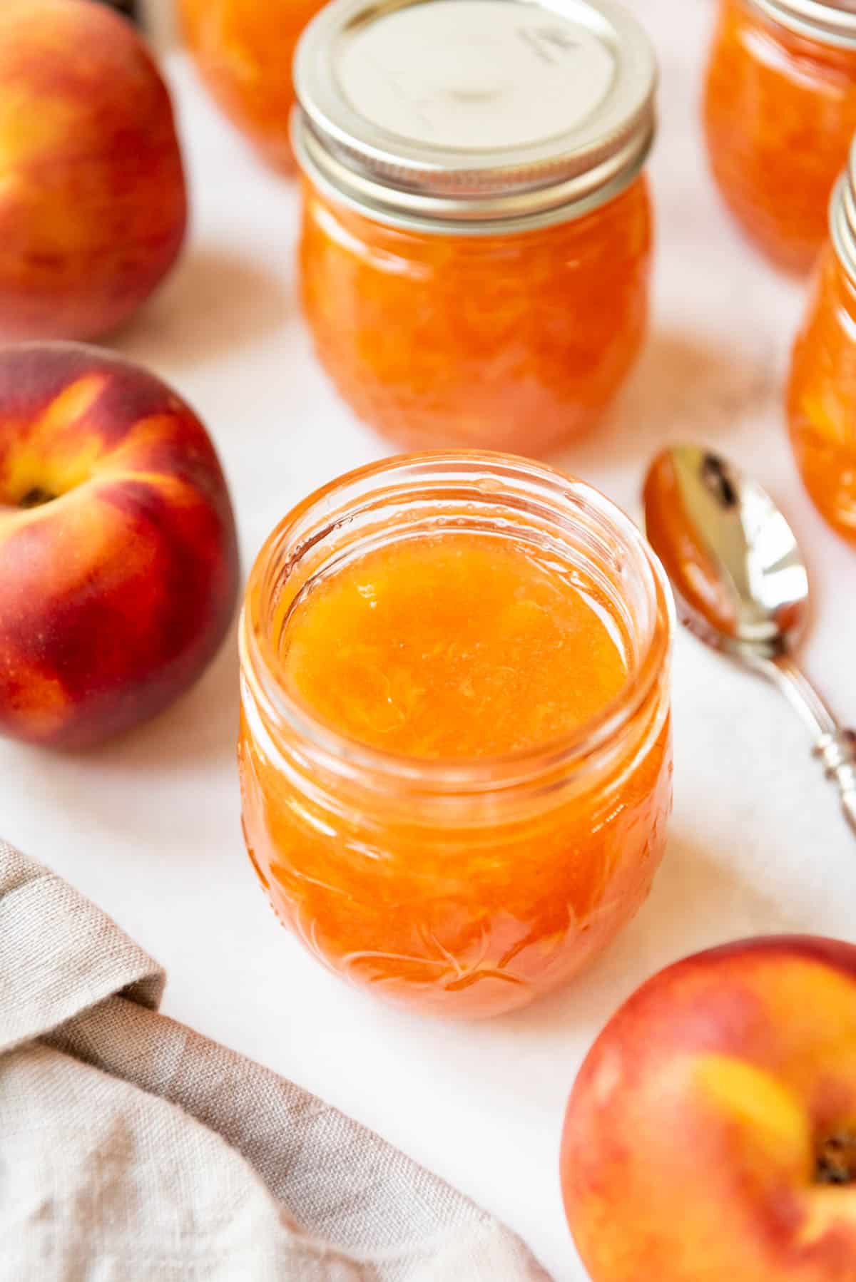 An overhead image of peach jam in a jar surrounded by more jam jars and fresh peaches.