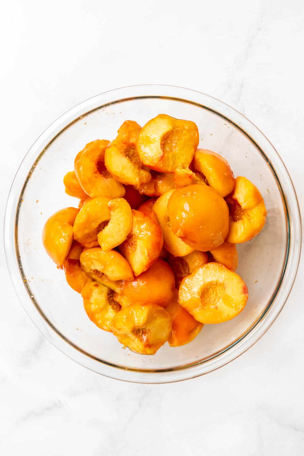 An overhead image of peeled and pitted peach halves in a bowl.