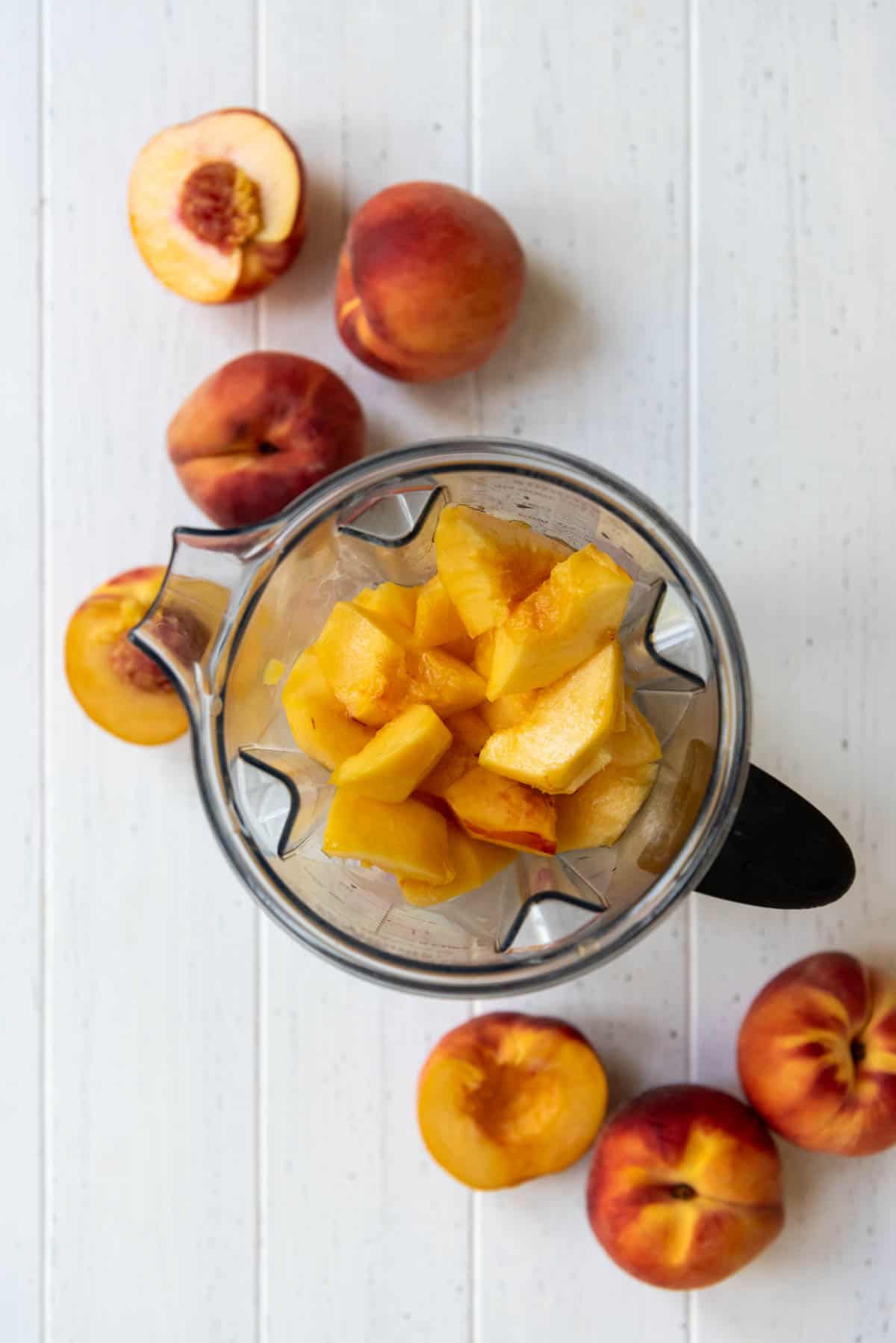 A blender pitcher full of ice cream and fresh sliced peaches.