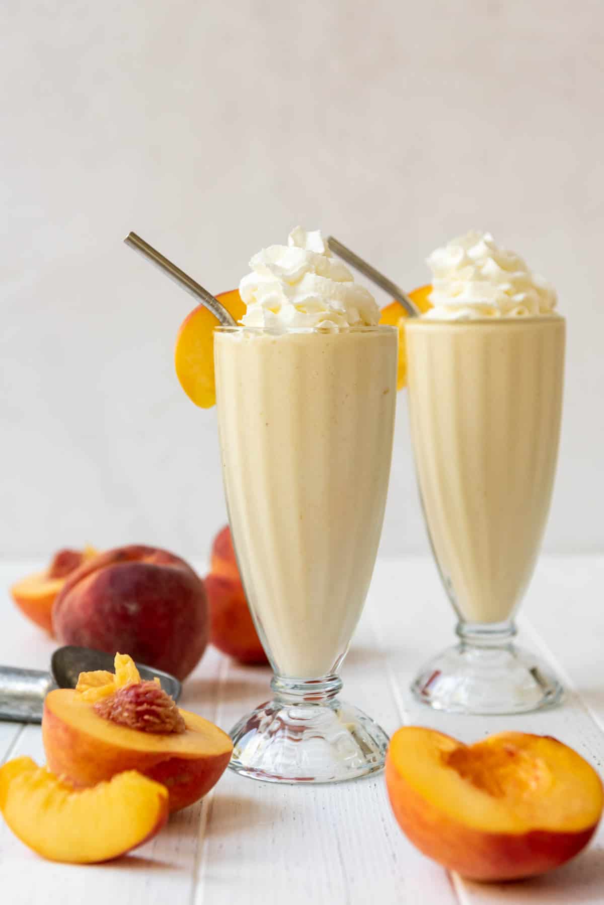 Two peach milkshakes in tall glasses surrounded by fresh peaches.