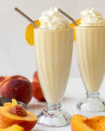 Two glasses of peach milkshake with whipped cream on top.