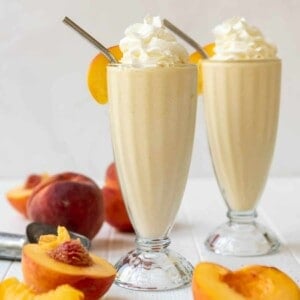 Two glasses of peach milkshake with whipped cream on top.