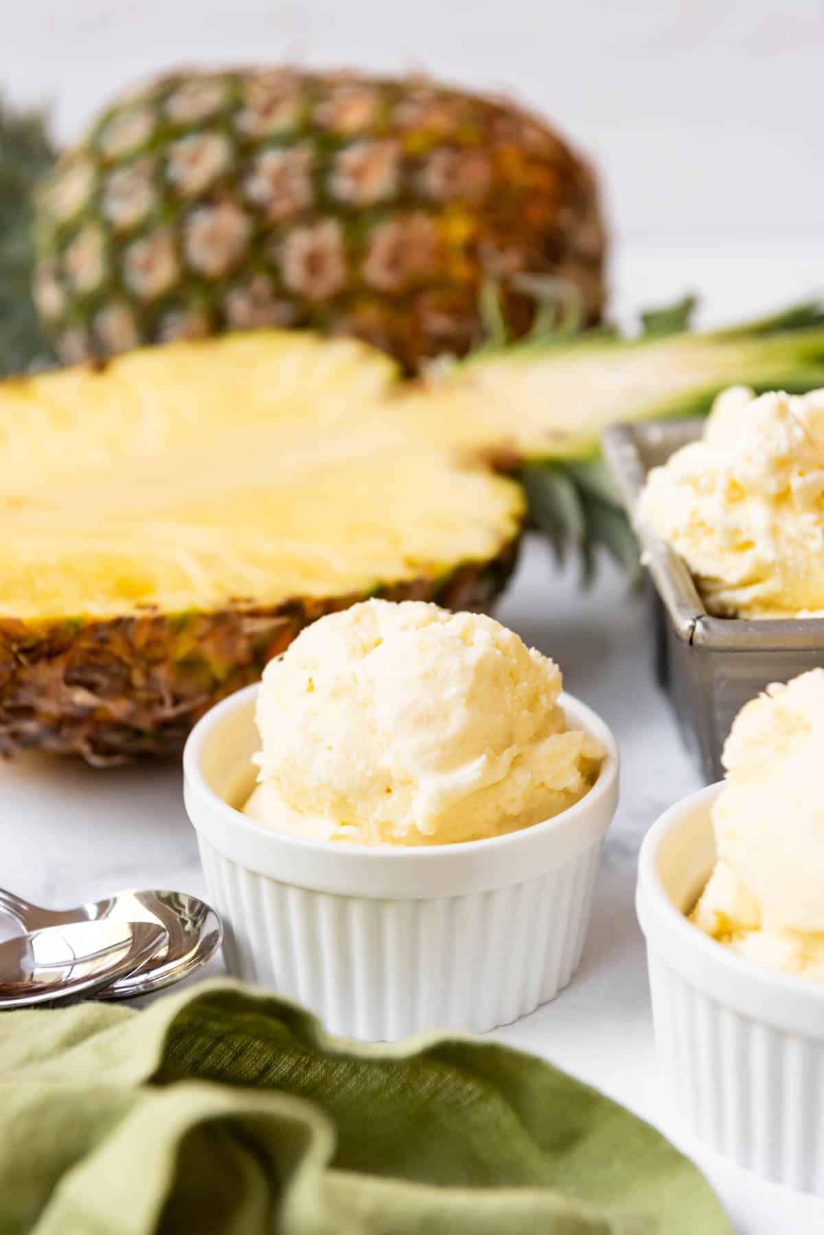 Bowls of pineapple ice cream in front of whole pineapples.