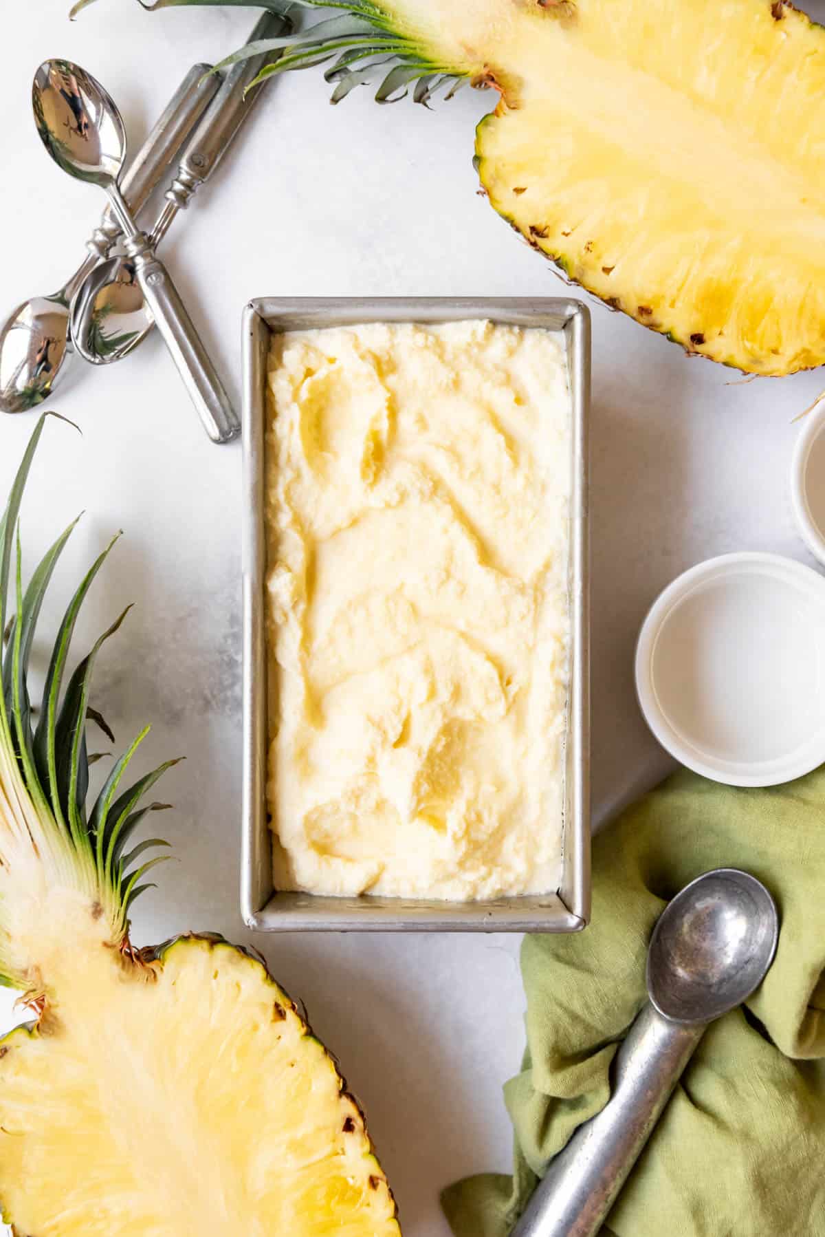 Homemade pineapple ice cream in a bread pan surrounded by fresh pineapple halves.