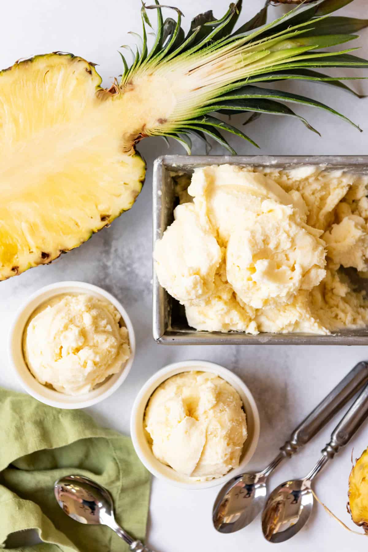 Scoops of fresh pineapple ice cream in bowls next to the container of homemade ice cream.