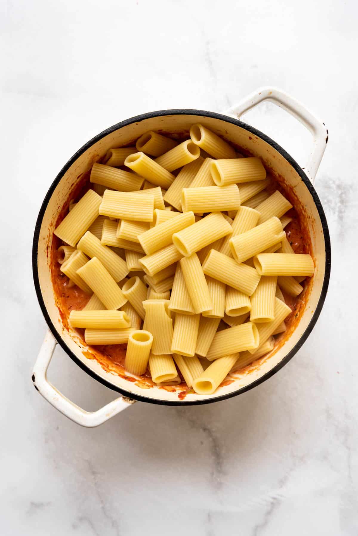Adding al dente rigatoni pasta to a meat sauce in a large pot.