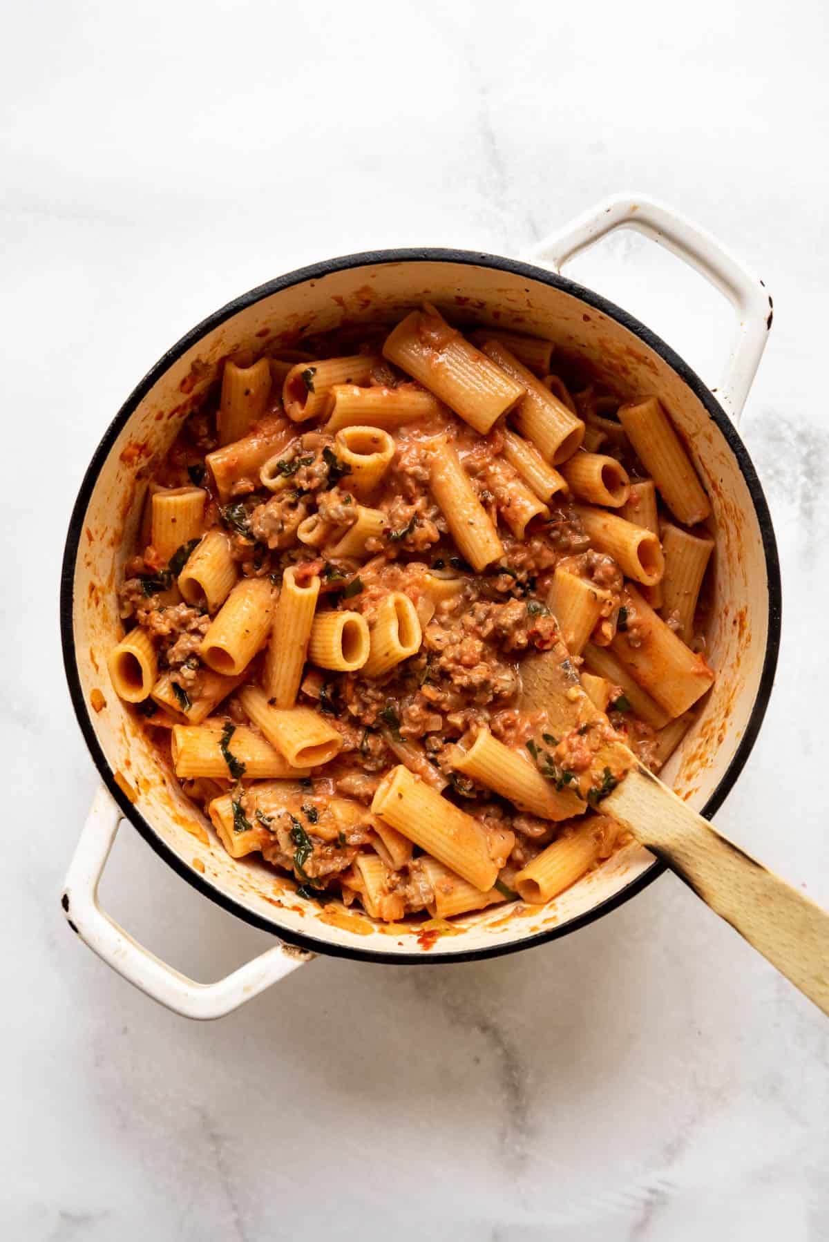Stirring cooked rigatoni pasta into a thick and meaty Italian sausage marinara sauce.